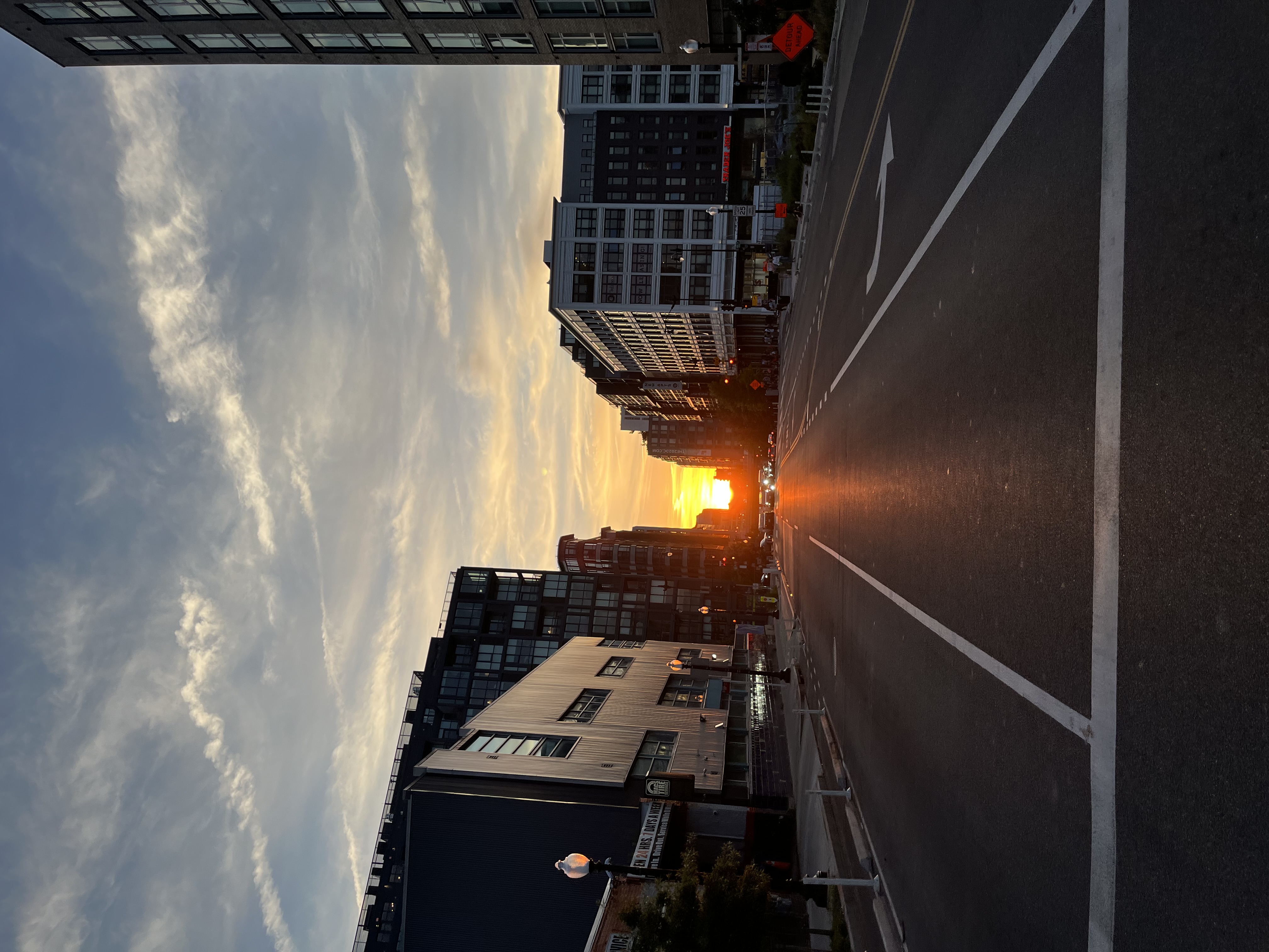A sunset image in Washington, DC. Taken down a metropolitan street, the building frames the sunset. The buildings appear dark grey. The sun appears orange.